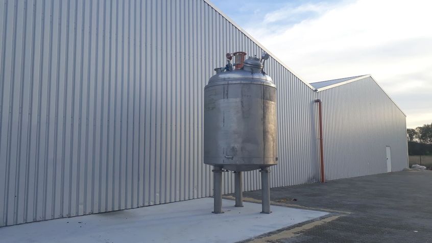 Edelstahl Tank auf Ständern vor einer modernen Lagerhalle.