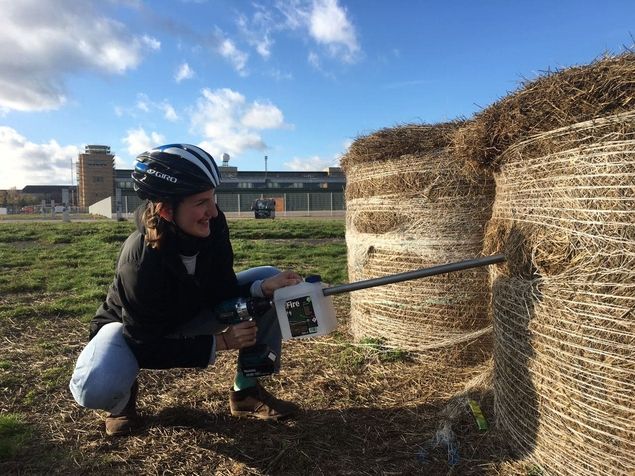 Frau in Helm bearbeitet Heuballen mit einer Bohrmaschine.